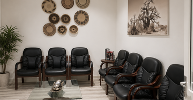 OB/GYN waiting room with black leather chairs, woven African basket wall art, a sepia baobab canvas, glass coffee table, and warm neutral finishes by NIZARRA.