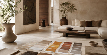 Warm Afro-modern living room with textured plaster walls, neutral furniture, natural wood, ceramic vessels, fabric samples, stone finishes, and colour palette swatches laid out for an interior design project.