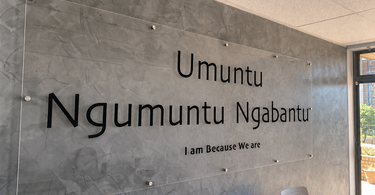 Matte glass Ubuntu signage by NIZARRA, mounted on a grey textured wall, featuring the words “Umuntu Ngumuntu Ngabantu” and “I am because we are.”