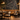 Sophisticated restaurant interior featuring NIZARRA Crossline 01 Charcoal wallpaper mural, warm tan banquette seating, bronze pendant lights and contemporary dining furniture.