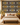 NIZARRA Ndebele-inspired wallpaper featuring ochre, ivory and burgundy geometric motifs on a black background, styled behind a neutral upholstered bed with timber bedside tables.