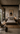 Afro-modern industrial bedroom with a low wooden platform bed, textured plaster walls, black wall sconces, abstract artwork, woven rug, leather chair, dark wood furniture, and warm neutral styling.