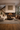 Luxury Afro-modern living room with textured plaster wall, central fireplace, sculptural furniture, and carved African wall art creating a warm, refined interior by NIZARRA.