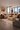 Refined Afro-modern living room in NIZARRA Urban Quiet style, featuring a neutral beige sectional sofa with layered textured cushions, sculptural travertine coffee table, dark wood side tables with ceramic lamps, and large abstract African-inspired wall art, set within a high-rise apartment with floor-to-ceiling windows and panoramic city views.