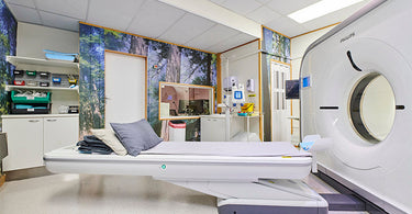 Wide view of an MRI scan room featuring a NIZARRA custom forest mural, patient scan table, medical storage, observation window, and MRI machine designed to create a calmer diagnostic environment.