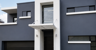 Wide view of a modern residential façade featuring grey and white walls, black doors, custom entrance shade, striped window frosting, and a clean front lawn.