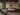 Afro-modern industrial bedroom with a low wooden platform bed, textured plaster walls, black wall sconces, abstract artwork, woven rug, leather chair, dark wood furniture, and warm neutral styling.