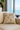 Beige pillow with black patterns on a beige sofa near a window with a view of water.
