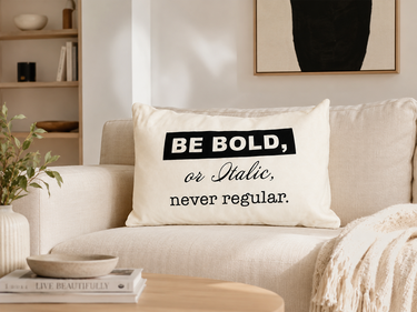 NIZARRA white “Be Bold, or Italic, never regular.” typography cushion styled on a cream sofa in a modern living room.