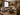 A warm Afro-modern living room featuring a light grey L-shaped sectional sofa, full-height taupe curtains, textured neutral walls, an arched recessed wall opening, three sculptural African shields, a rounded walnut coffee table, layered neutral rug, indoor plants, and earthy ceramic décor.