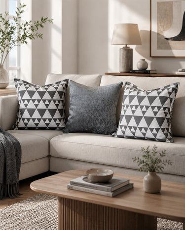 Neutral living room sofa styled with two grey and white geometric triangle NIZARRA Xhosa-inspired cushions and a textured grey cushion in an Afro-modern interior setting.