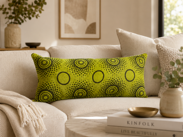 Lime green NIZARRA Setswana-inspired lumbar cushion styled on a soft cream sofa in a warm, refined living room.