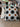 NIZARRA dot pattern cushion photographed on a textured sofa, featuring black halftone circles and warm brown circular accents on a cream woven fabric base.