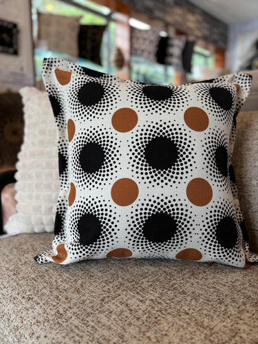 NIZARRA dot pattern cushion photographed on a textured sofa, featuring black halftone circles and warm brown circular accents on a cream woven fabric base.