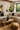 Modern boho living room with a cream sectional sofa styled with black and cream mud cloth-inspired NIZARRA cushions, natural wood furniture, woven textures, indoor plants, and warm sunlight.
