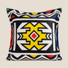 Square NIZARRA Ndebele-inspired cushion with bold black and white geometric patterns, a yellow central motif, red diamond detail, and blue and green accents on a cream background.