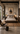 Contemporary African bedroom interior with a low timber bed, neutral bedding, geometric wall art, textured rug, black metal lighting, natural wood furniture and warm earthy styling.
