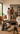 Couple standing in a partially furnished living room with moving boxes, furniture, cushions and a rolled rug while considering how to arrange and complete the space.