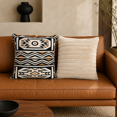 Black, cream and ochre Ndebele-print cushion paired with a cream ribbed faux-fur cushion on a tan leather sofa.