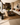 NIZARRA Afro-modern living room with beige sectional sofa, earthy cushions, woven rug, dark wood coffee table, abstract wall art and natural light from large windows.