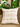 Cream and beige Sepedi-inspired NIZARRA cushion styled on a neutral chair beside lush green indoor plants.
