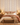 NIZARRA Strata geometric striped wallpaper behind an upholstered bed in a contemporary bedroom, featuring ochre, warm grey and burgundy motifs with natural wood furniture and earthy bedding.