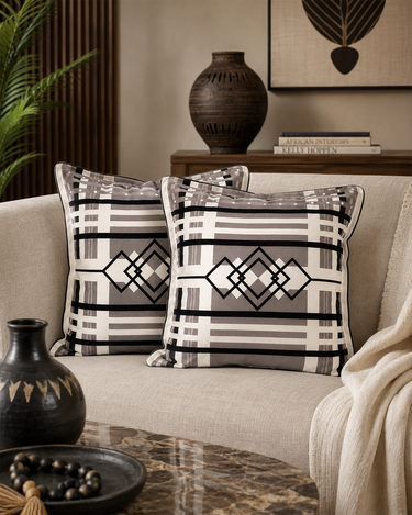 Two NIZARRA Venda-inspired geometric cushions styled on a soft neutral sofa in an Afro-modern living room.
