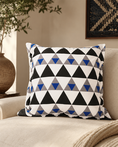 NIZARRA Xhosa-inspired geometric cushion in black, white, grey and cobalt blue styled on a textured cream armchair with warm natural accents.