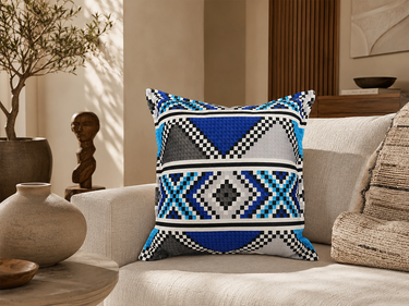 Blue, black, grey and white Zulu bead-inspired NIZARRA cushion featured on a textured cream armchair in a refined modern living space.