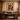 Afro-modern executive office interior featuring a large dark wood desk and built-in shelving, with a framed African warrior artwork centered on a warm textured plaster wall, softly lit with ambient lighting and neutral earthy tones.